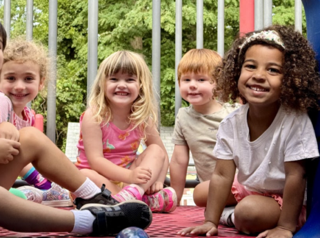 Preschool students sitting together on the playground equipment smiling for a picture